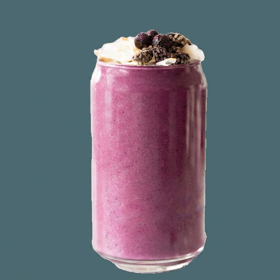 Tall glass of purple berry smoothie topped with whipped cream, berries, and chocolate cereal against a blue background.